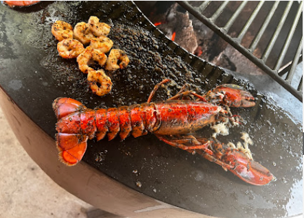 Langosta y gambas rojas sobre el acero de la parrilla circular con brasas