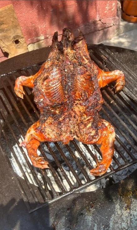 Pollo entero abierto dorándose en la parrilla circular